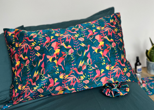Lively Hummingbird silk pillowcase and scrunchie on a bed.