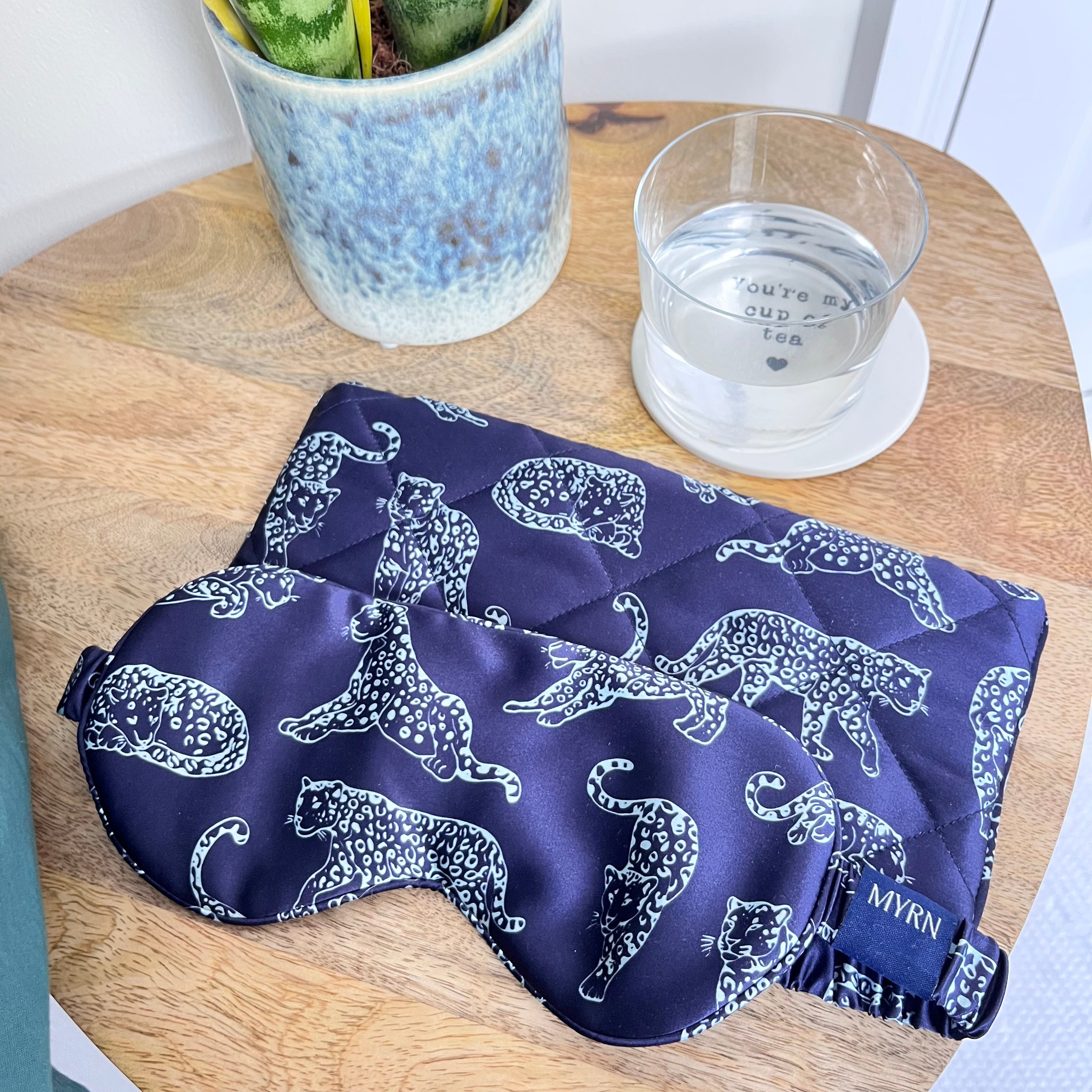 MYRN Midnight Blue Leopard Printed Silk eye mask with matching travel case on a bedside table