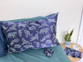 Midnight Leopard silk pillowcase, scrunchie on a bed and eye mask and travel pouch on a bedside table