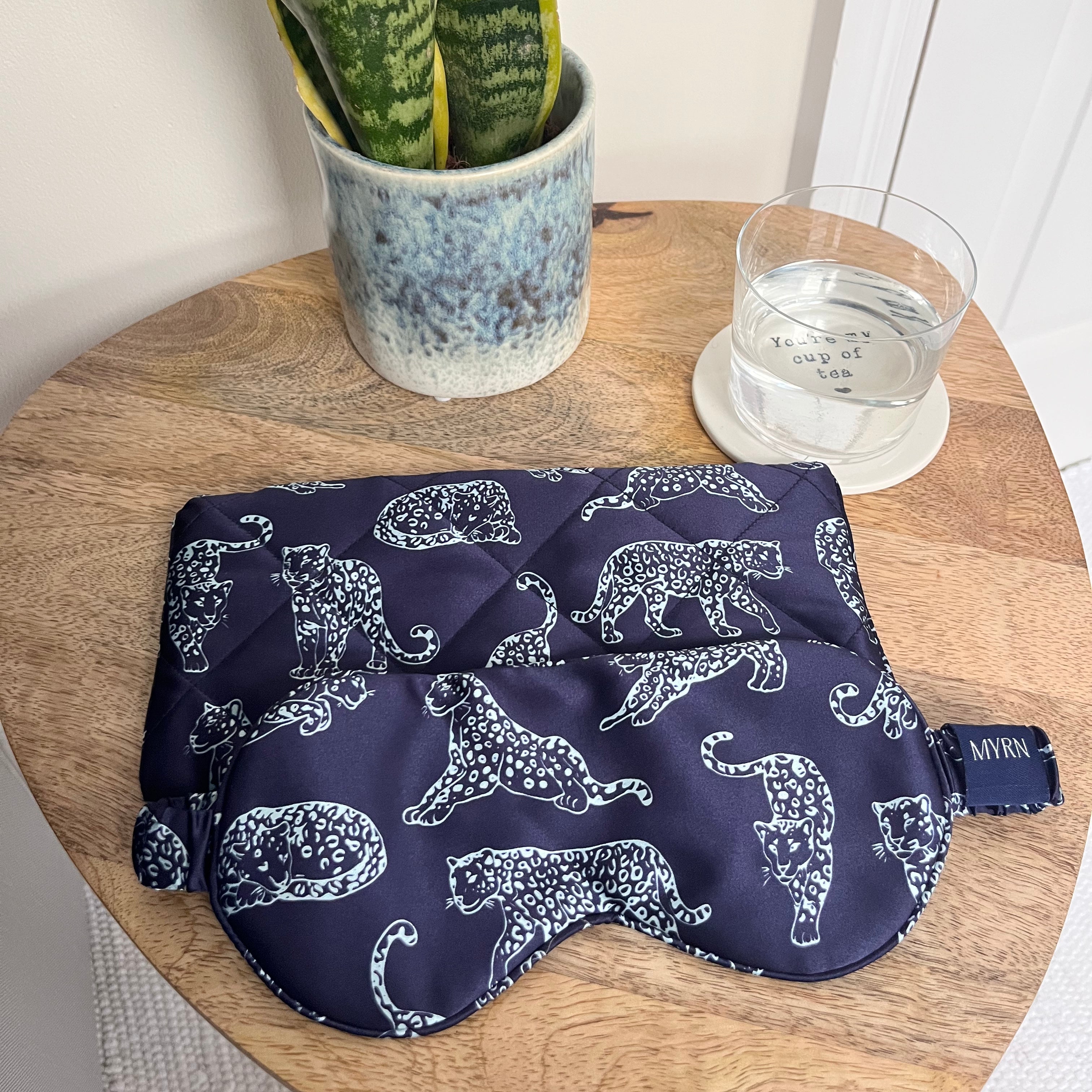 MYRN Midnight Blue Leopard Printed Silk eye mask with matching travel case on a bedside table