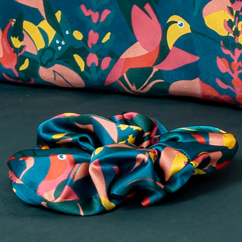 Close up of a hummingbird printed silk scrunchie on a bed